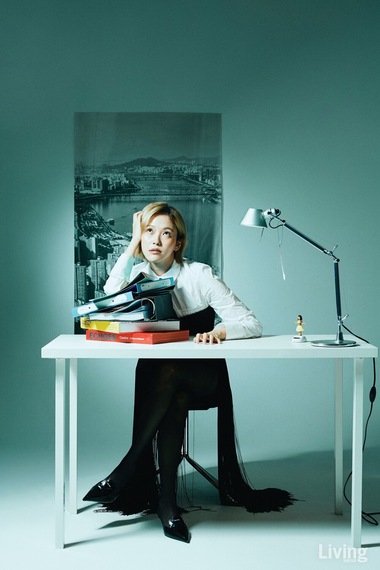 화이트 셔츠는 자라@Zara, 뷔스티에와 스커트, 슬링백 힐은 모두 프라다 @prada.  포스터는 한동원 @_handongwon 작가의 사진.  카페 ‘이치 서울’에서 볼 수 있다. 스틸 프레임 체어는 텍스쳐 @txture.kr.